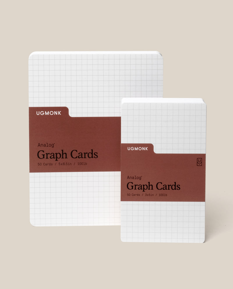 Two packs of Ugmonk Analog Graph Cards are shown upright. Both have a white grid design and a brown label. The larger pack is 5x6.5 inches, the smaller is 3x5 inches. Each contains 50 cards.