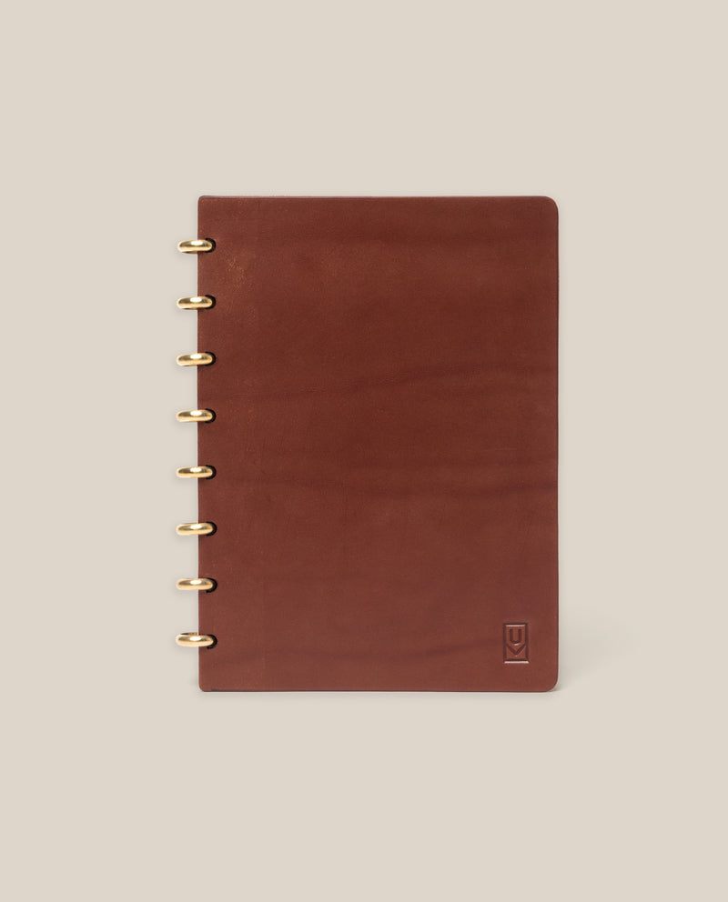 The Discbound Heirloom Journal (Brown Leather, 6" x 8.5") features refillable pages, gold disc binding, and a subtle embossed logo in the bottom right corner, shown on a plain beige background.