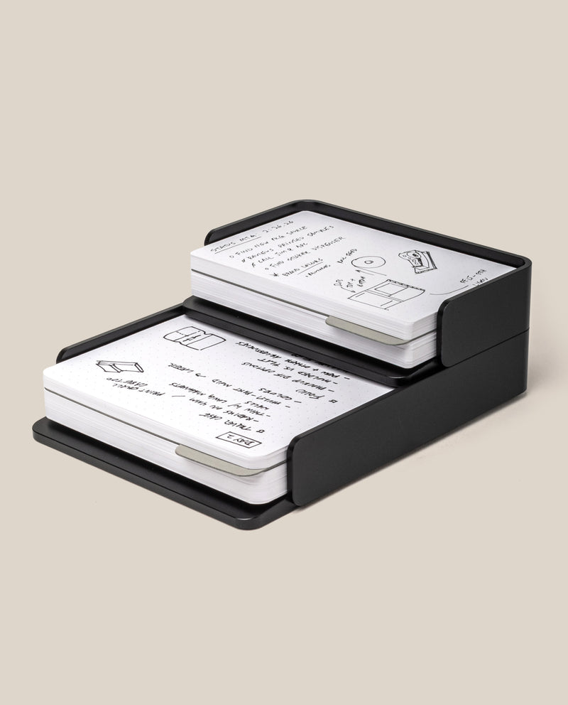 A black Analog Capture Kit - Small & Large (Black Aluminum) holds stacks of Dot Grid Cards featuring black handwritten notes and simple illustrations on a beige background.