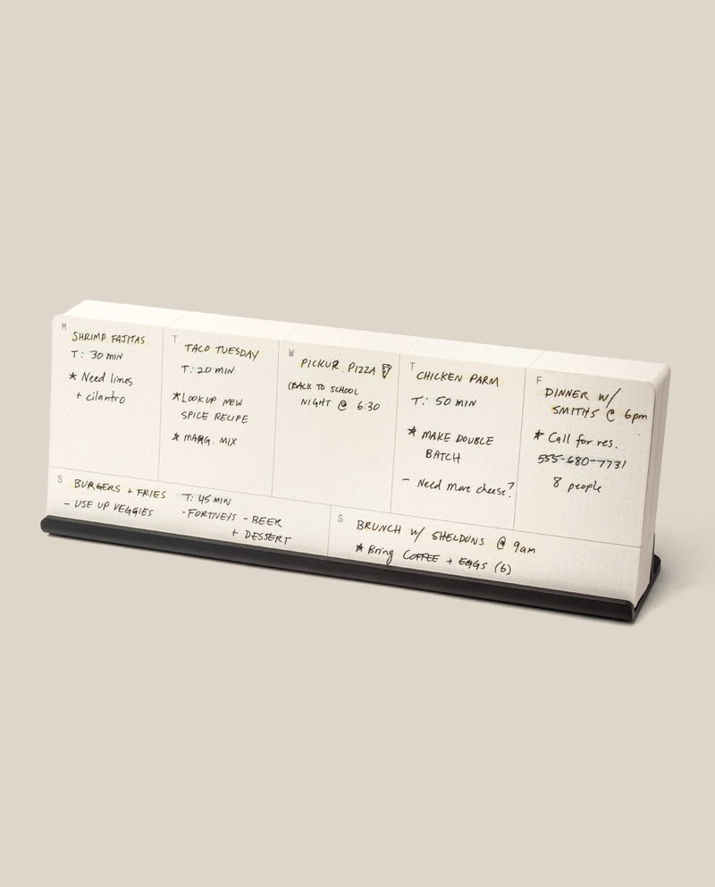 The Analog Weekly Planning Kit (Black Aluminum) is a desktop planner with seven sections for each day, labeled for meal ideas, ingredients, cooking times, and notes. It features a sleek black aluminum base for stylish organization.