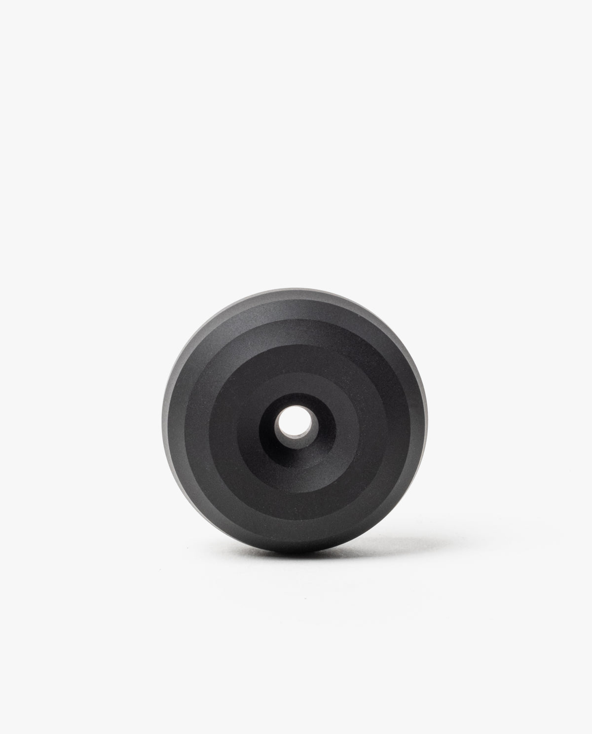 The HMM Paperweight Pen Stand (Black) is a circular aluminum piece with concentric raised rings and a central hole, shown on a plain white background.