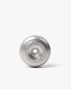 A modern desk accessory, the HMM Paperweight Pen Stand (Raw) features a metallic, circular design with concentric rings and a central hole. Crafted from sleek aluminum, it stands upright on a white background, serving as both an elegant paperweight and a stylish pen stand.