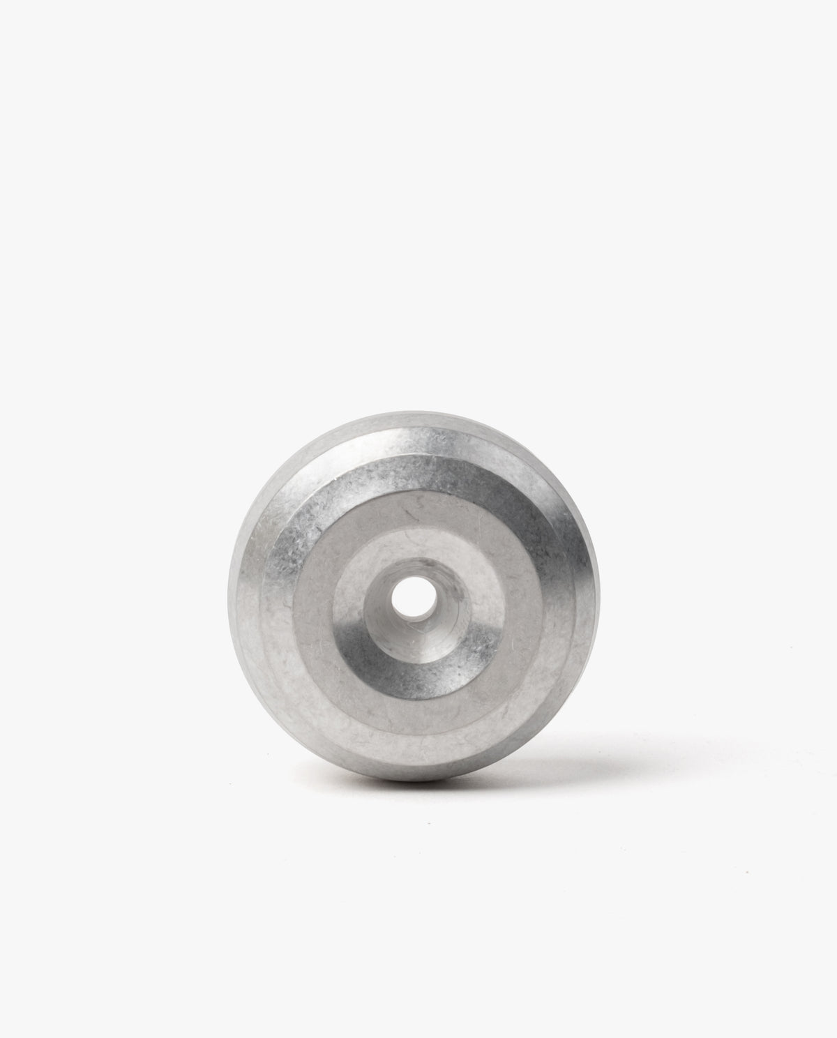 A modern desk accessory, the HMM Paperweight Pen Stand (Raw) features a metallic, circular design with concentric rings and a central hole. Crafted from sleek aluminum, it stands upright on a white background, serving as both an elegant paperweight and a stylish pen stand.