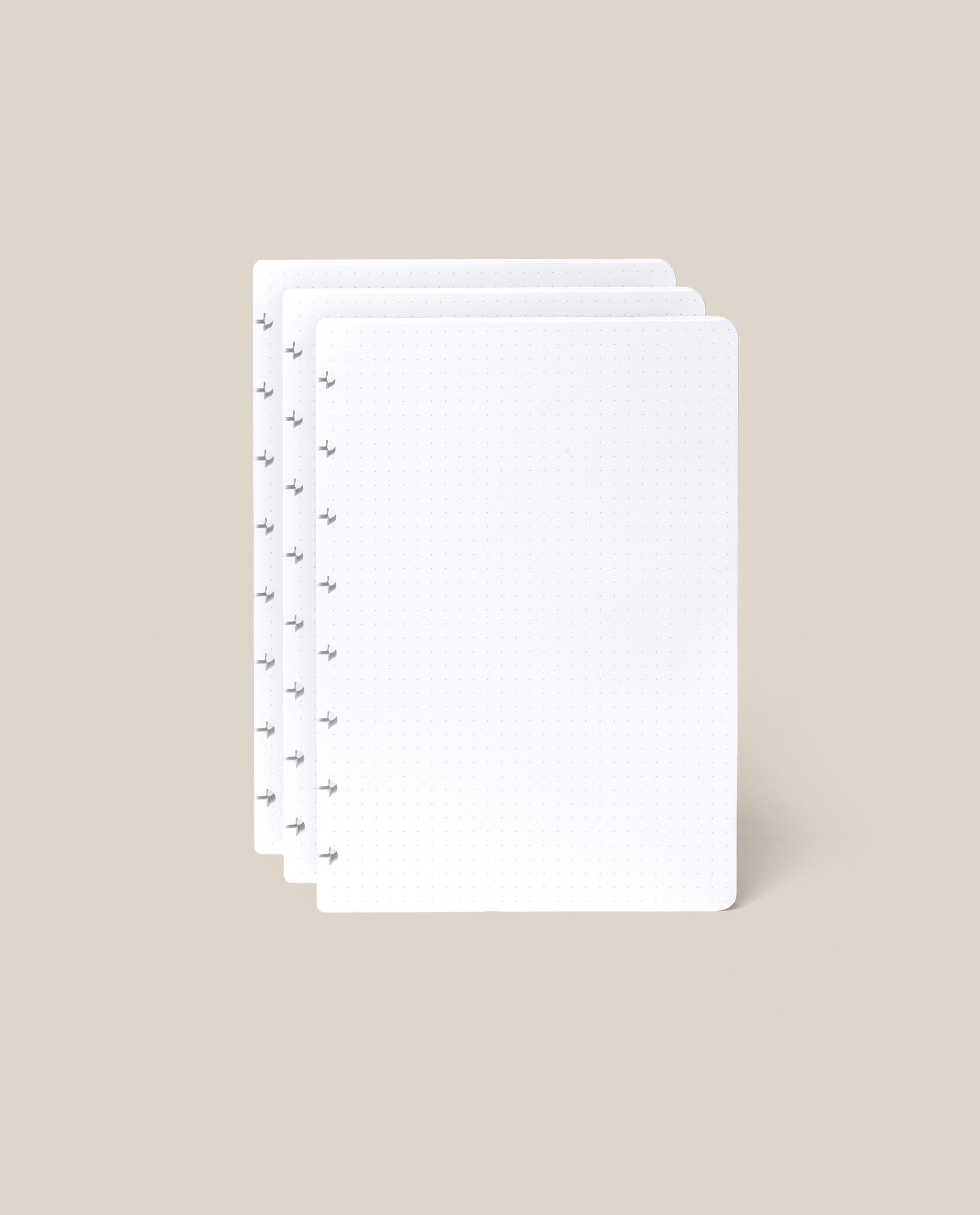 Three stacked sheets from the Discbound Journal Refill (Standard 6" x 8.5" – 3-Pack), featuring a white dot grid and circular holes along the left edge, displayed on a light beige background—ideal for discbound notebooks.