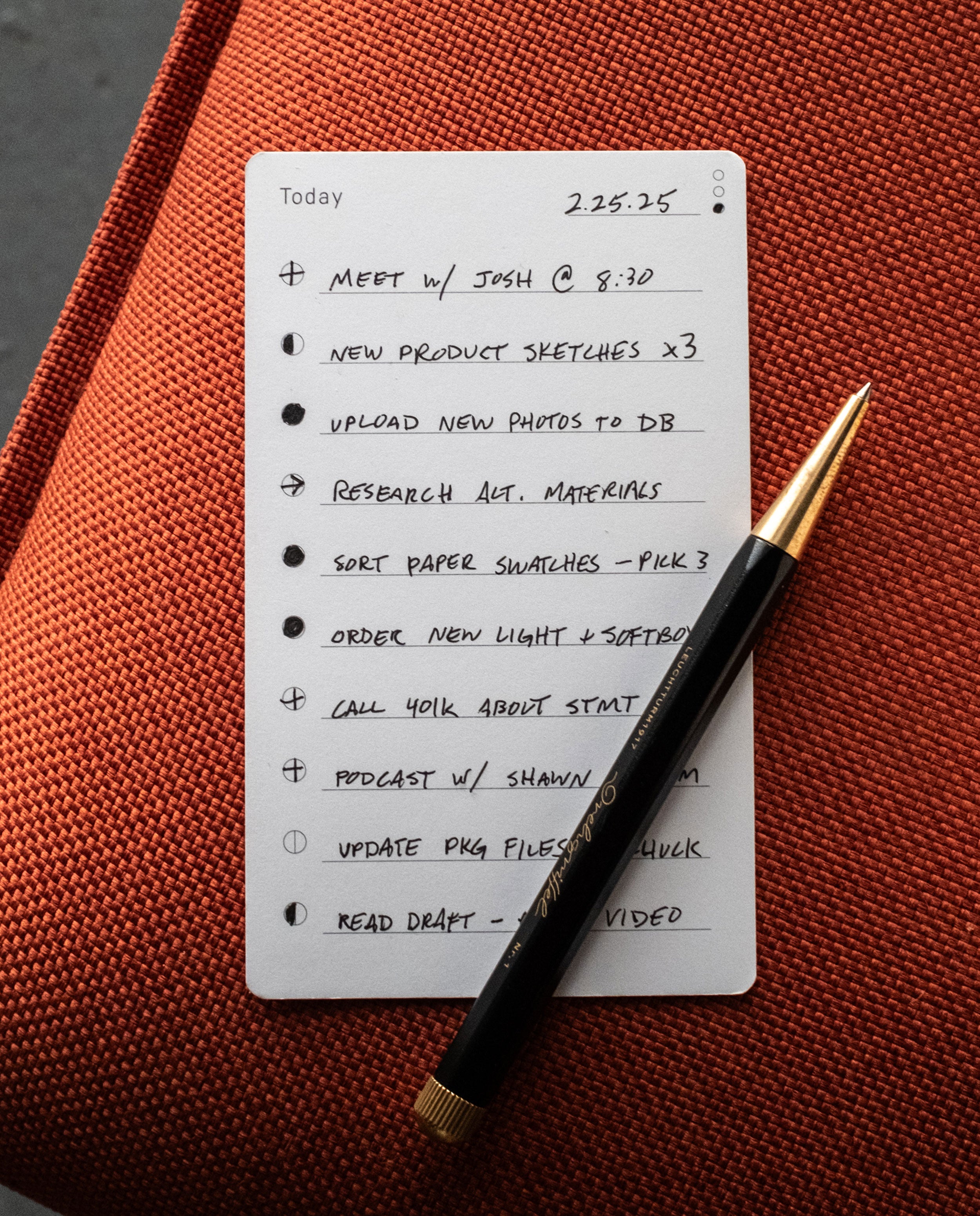 An Analog Task Cards - Small notepad, with a black and gold pen resting on top, sits on an orange textured surface. Similar to productivity cards from the Analog system, it features a to-do list with tasks like meetings, uploads, research, shopping, and calls—most already checked off for convenience.