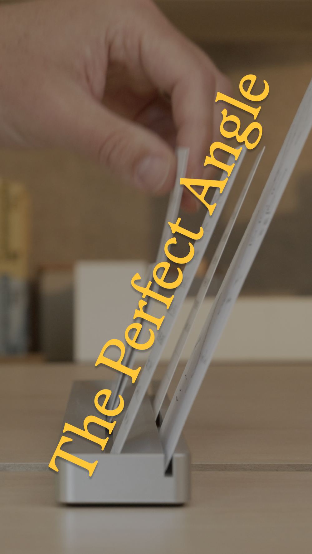 A hand adjusts a thin device propped up at an angle on a silver stand. Large yellow text across the image reads “The Perfect Angle.”.