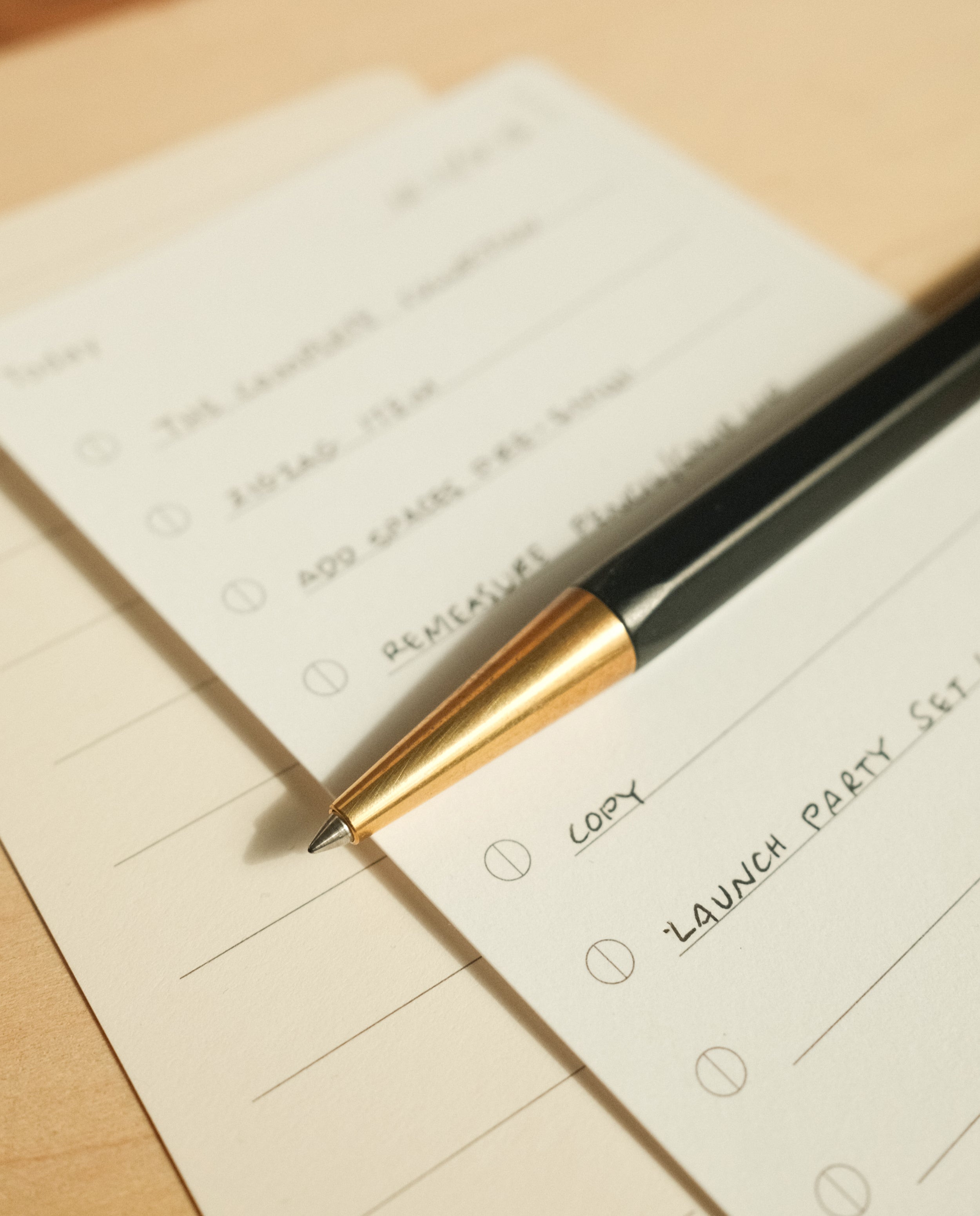 The Ugmonk Pen (Leuchtturm1917 Drehgriffel - Black) rests on a to-do list with handwritten tasks and empty checkboxes on lined paper atop a light wooden surface.