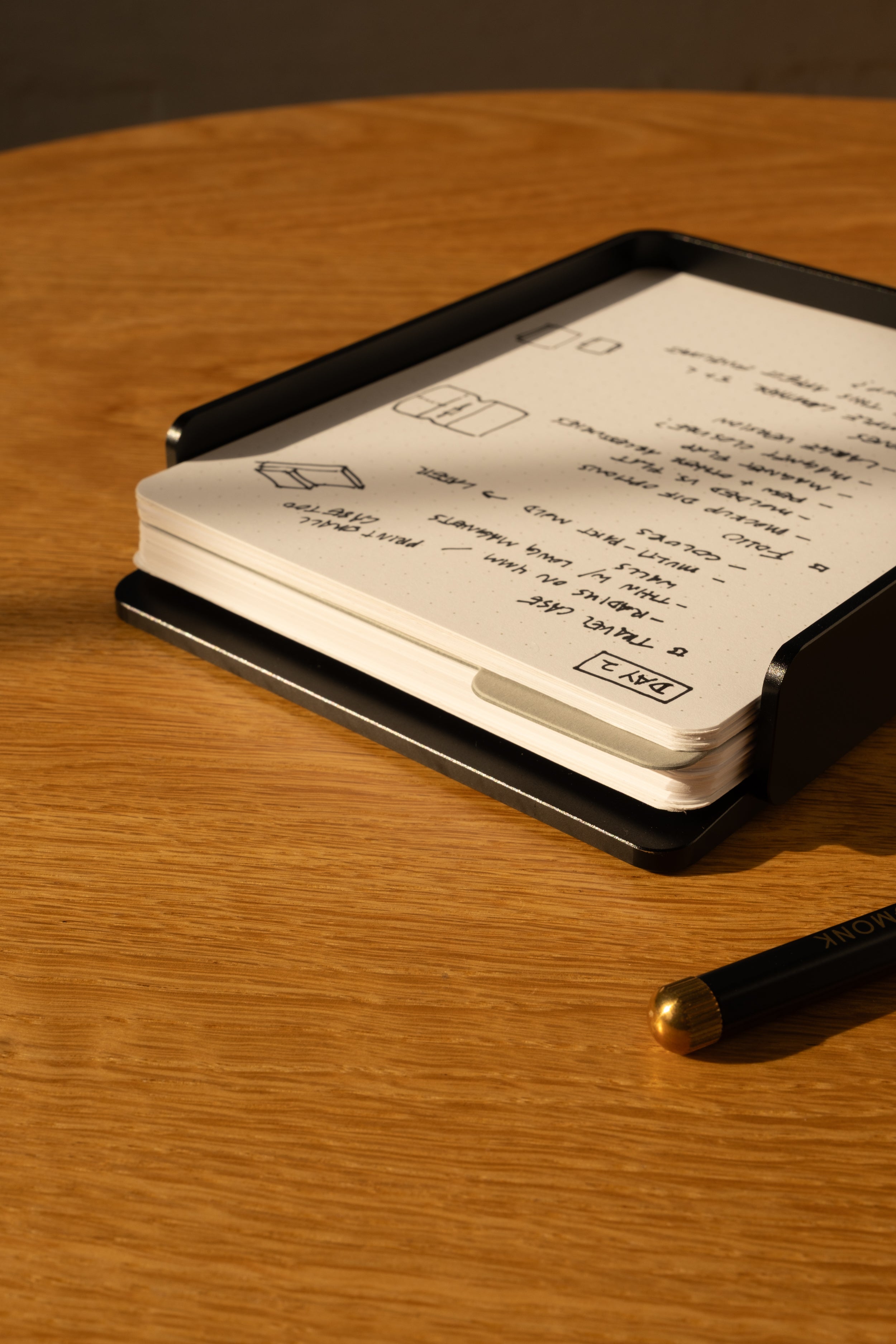 The Analog Capture Kit - 2 Large (Black Aluminum) sits on a wooden table, holding a stack of dot grid cards filled with handwritten black ink notes and drawings. A black pen rests nearby.