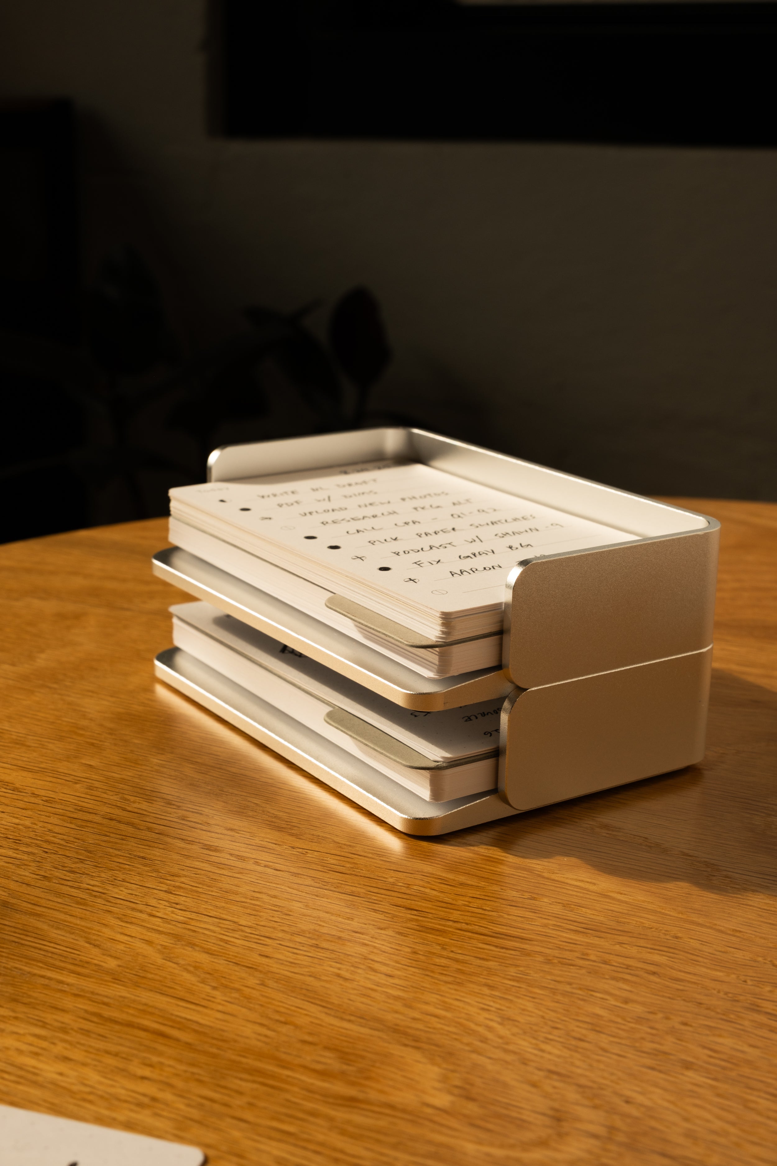 A stack of handwritten cards from the Analog Capture Kit - Small (Silver Aluminum) sits in its sleek tray on a wooden table, bathed in sunlight—perfect for capturing inspired thoughts.