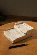 The Analog Capture Kit - Small (Silver Aluminum) with dot grid cards sits on a wooden table. A black and gold pen lies in front, while warm sunlight highlights the inviting setup, perfect for capturing hand-drawn diagrams and notes.