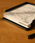 The Analog Capture Kit - Large (Black Aluminum) includes large dot grid cards in a sleek black holder, with a black pen featuring a gold tip, all resting on a wooden surface—an ideal setup for your notes.