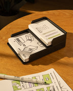 The Analog Capture Kit - Small & Large (Black Aluminum) rests on a wooden table beside an open notebook with colorful sketches and a green marker, as sunlight casts warm shadows over this creative setup.