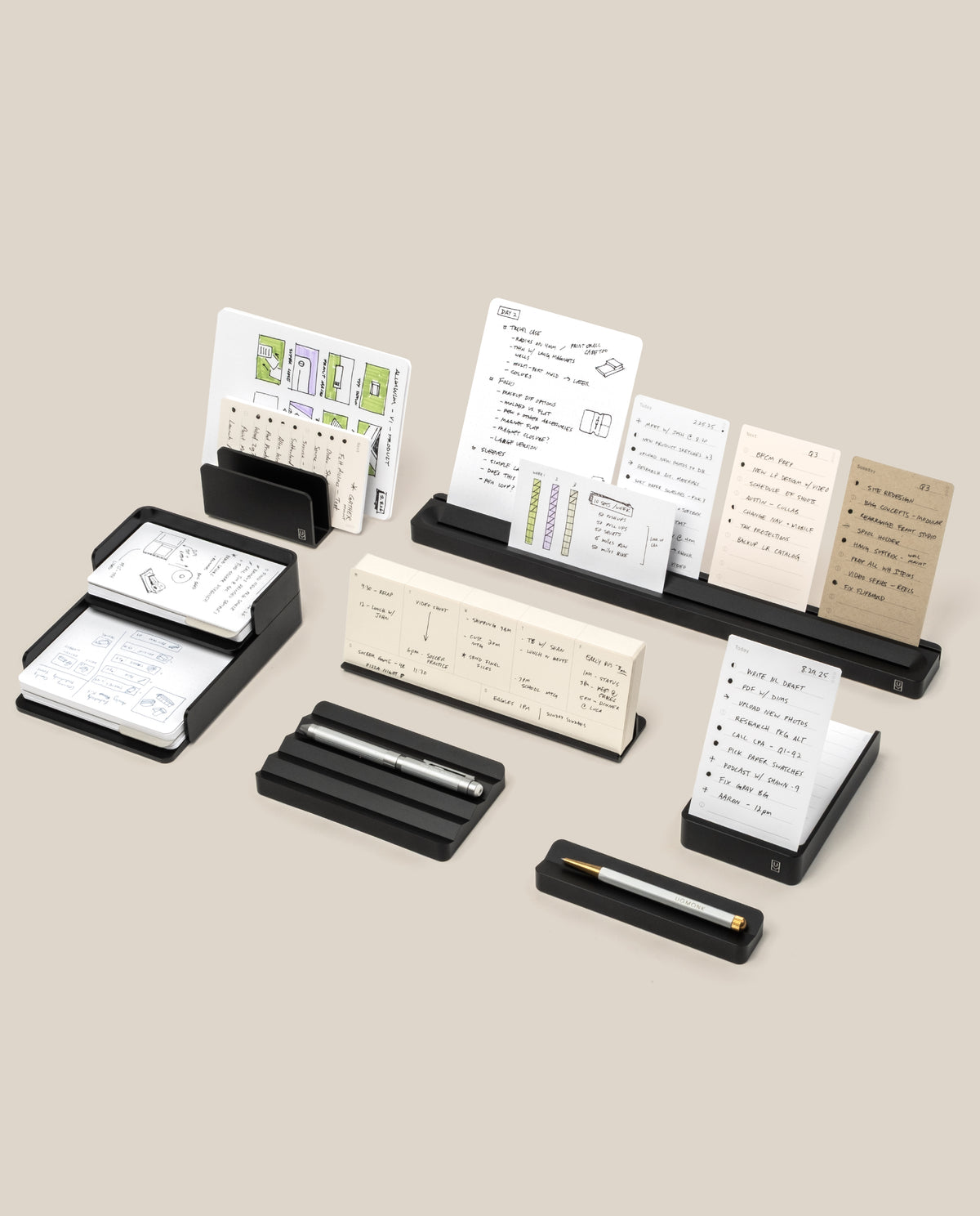 The Complete Analog Collection (Black Aluminum) organizes notepads, index cards, and pens neatly on a beige background, showcasing handwritten notes and diagrams.