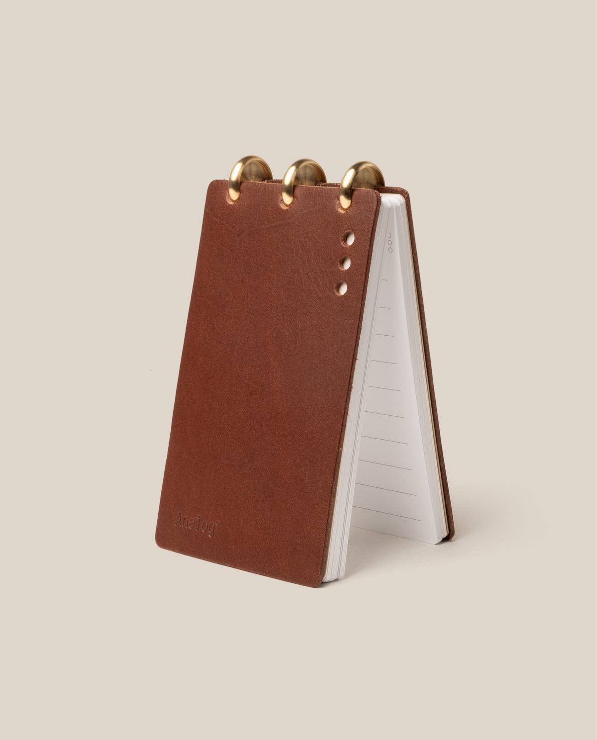 The Leather Discbound Analog (Brown) is a compact notepad with full-grain leather covers, subtle embossed text, three gold discs at the top, four small holes, and lined pages—ideal for use with Analog Task Cards.
