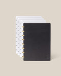 The Discbound Heirloom Journal Bundle (Black Leather - Standard 6" x 8.5" + 3 Refills) is open with gold rings, showing dotted and patterned pages fanned out behind the cover on a light beige background.