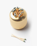 The Craighill Match Striker (Brass) is a gold, round solid brass holder filled with wooden matches, with three strike anywhere matches placed beside it on a white surface.