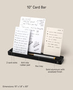 The Analog Card Bar (Small 10" - Black) is a solid aluminum desk organizer with two card slots to hold three notes upright, a pen tray, labeled features for easy use, anti-slip pad, and durable build. Dimensions: 10 × 1.8 × .63 inches.