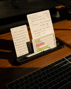 Sunlight illuminates handwritten notes with a to-do list and diagram, propped in the Analog Card Bar (Small 10" - Black) solid aluminum card holder, alongside a silver pen and part of a laptop keyboard.