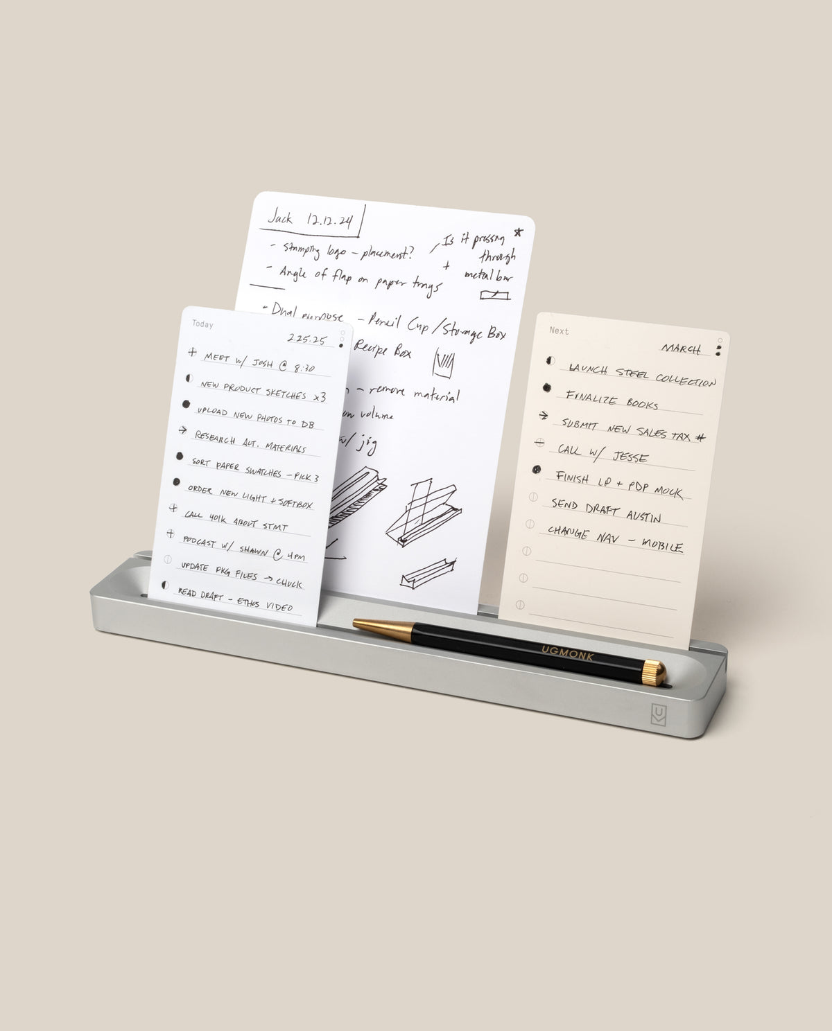 A silver Aluminum Analog Card Bar - Essentials Kit holds a black pen and three dot grid cards featuring handwritten notes, sketches, and to-do lists. The task cards stand upright in the slots of the Card Bar against a plain beige background.