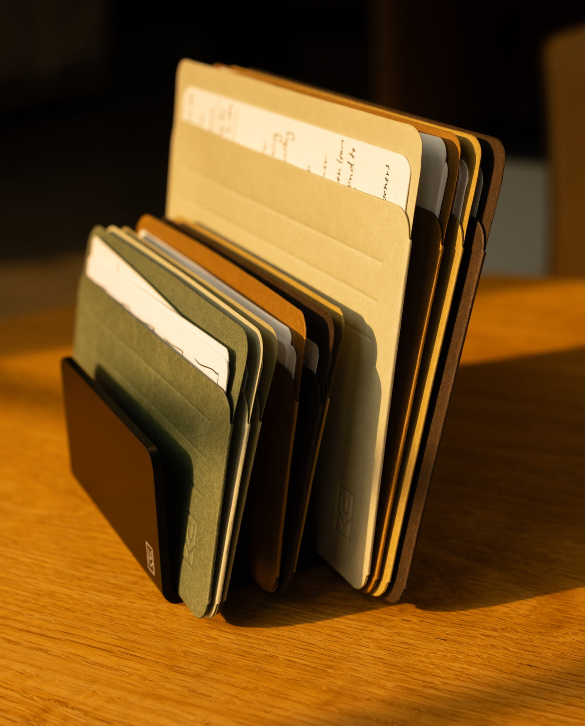 A set of assorted folders and documents, together with Analog Card Sleeves - Large (Earth), is organized in a vertical file holder that sits on a wooden desk, warmly illuminated by sunlight.
