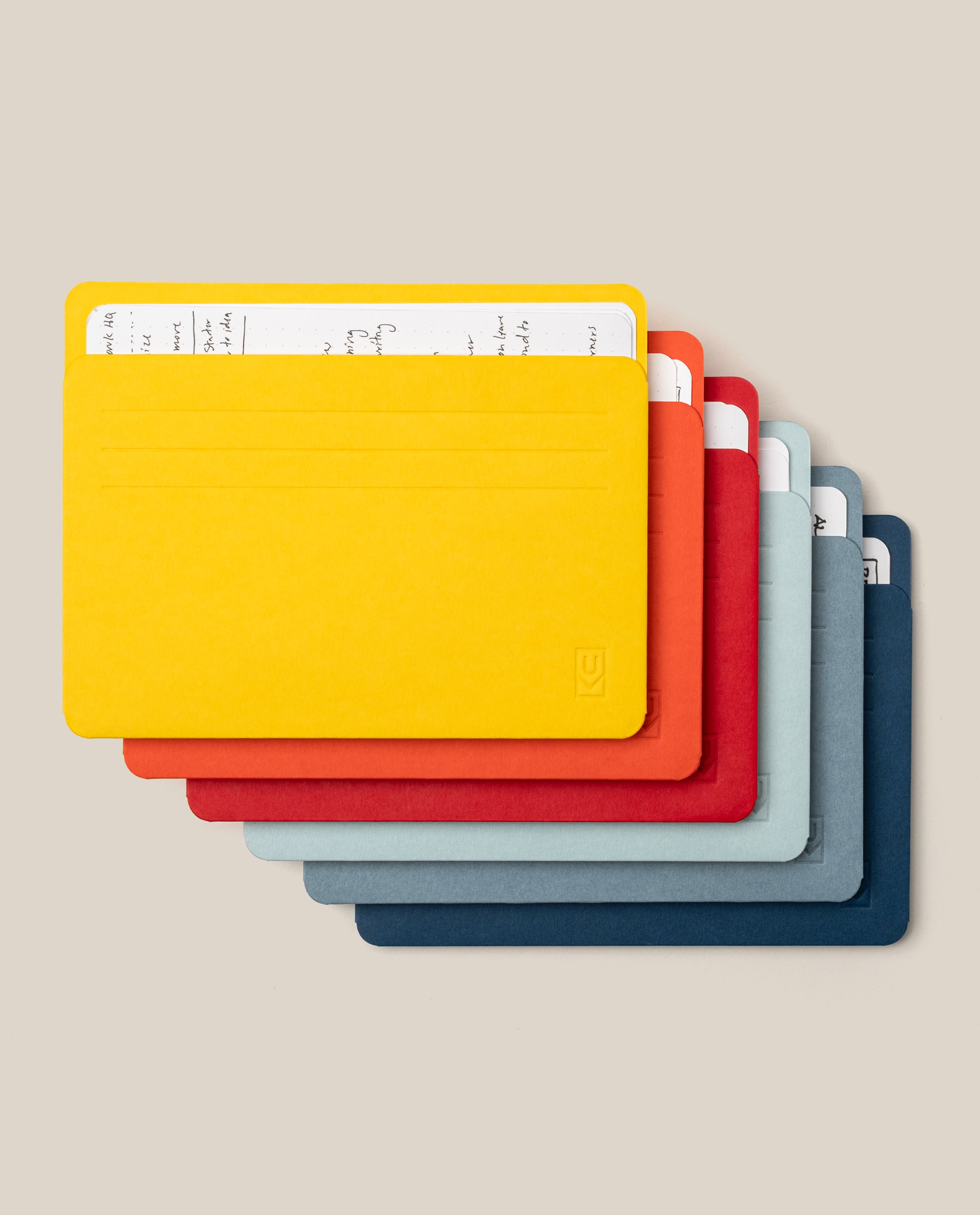 Seven colorful index cards—yellow, red, orange, dark gray, light gray, blue, and navy—are stacked askew with the yellow card on top partially revealing handwritten notes beneath. They fit neatly into the Analog Card Sleeves - Large (Bright), a practical organizer that keeps your notes secure and easily accessible.