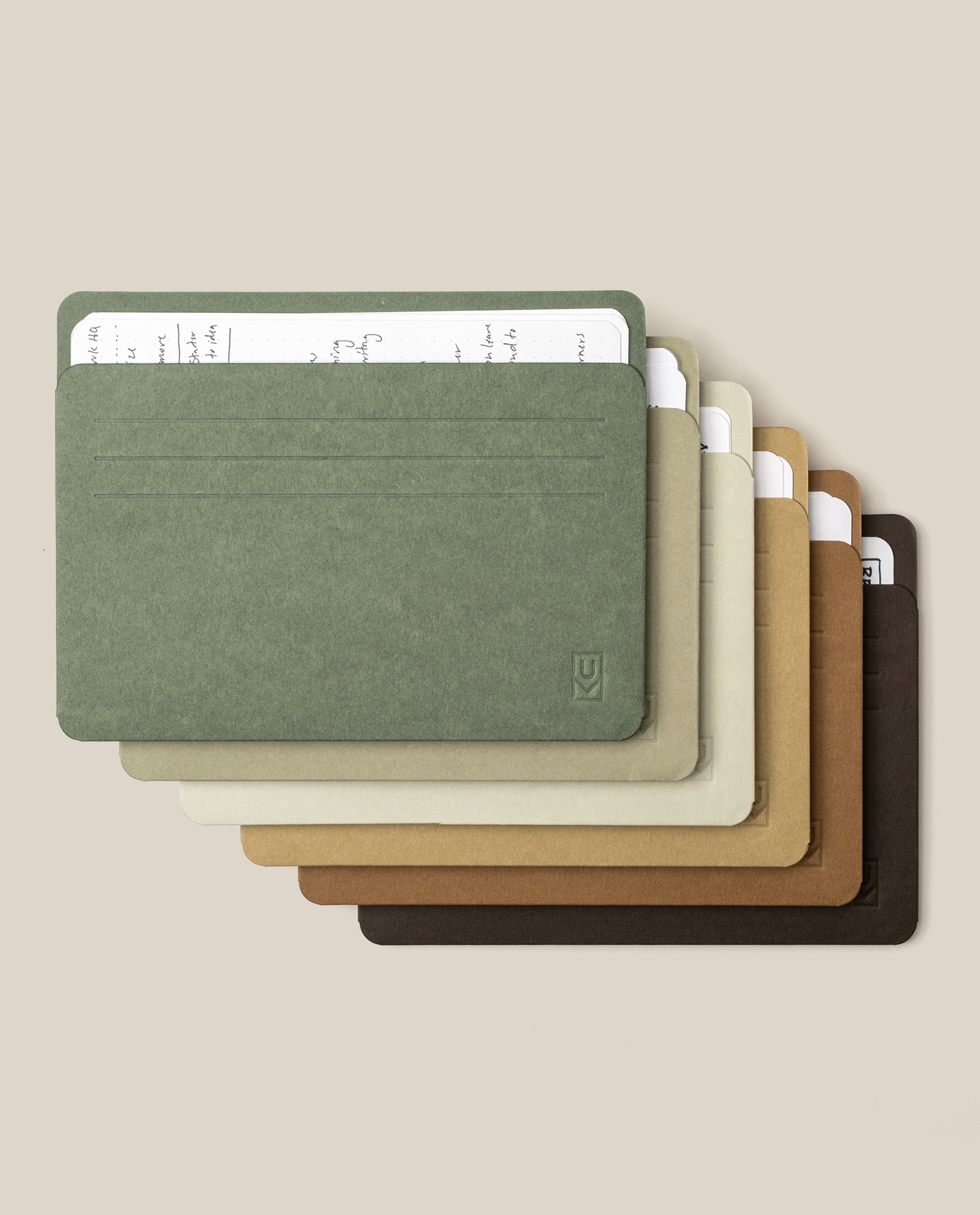 Six Analog Card Sleeves - Large (Earth) in assorted earthy hues are neatly stacked, each elegantly organizing a handwritten index card on lined paper. The sleeves fan out across a beige background, beautifully highlighting their blend of style and practicality for keeping your favorite notes or durable card stock in order.
