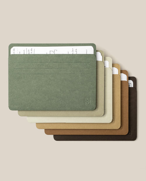 Six Analog Card Sleeves - Large (Earth) in assorted earthy hues are neatly stacked, each elegantly organizing a handwritten index card on lined paper. The sleeves fan out across a beige background, beautifully highlighting their blend of style and practicality for keeping your favorite notes or durable card stock in order.