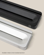 Two minimalist Analog Card Bars (Small 10” – Silver), one in black and one in silver, rest diagonally on a light background. Each solid aluminum stand functions as both a card holder and pen tray, with a central groove and a small corner logo for subtle branding. The text below highlights their availability in black or silver anodized aluminum—making them an ideal desk organizer for modern workspaces.