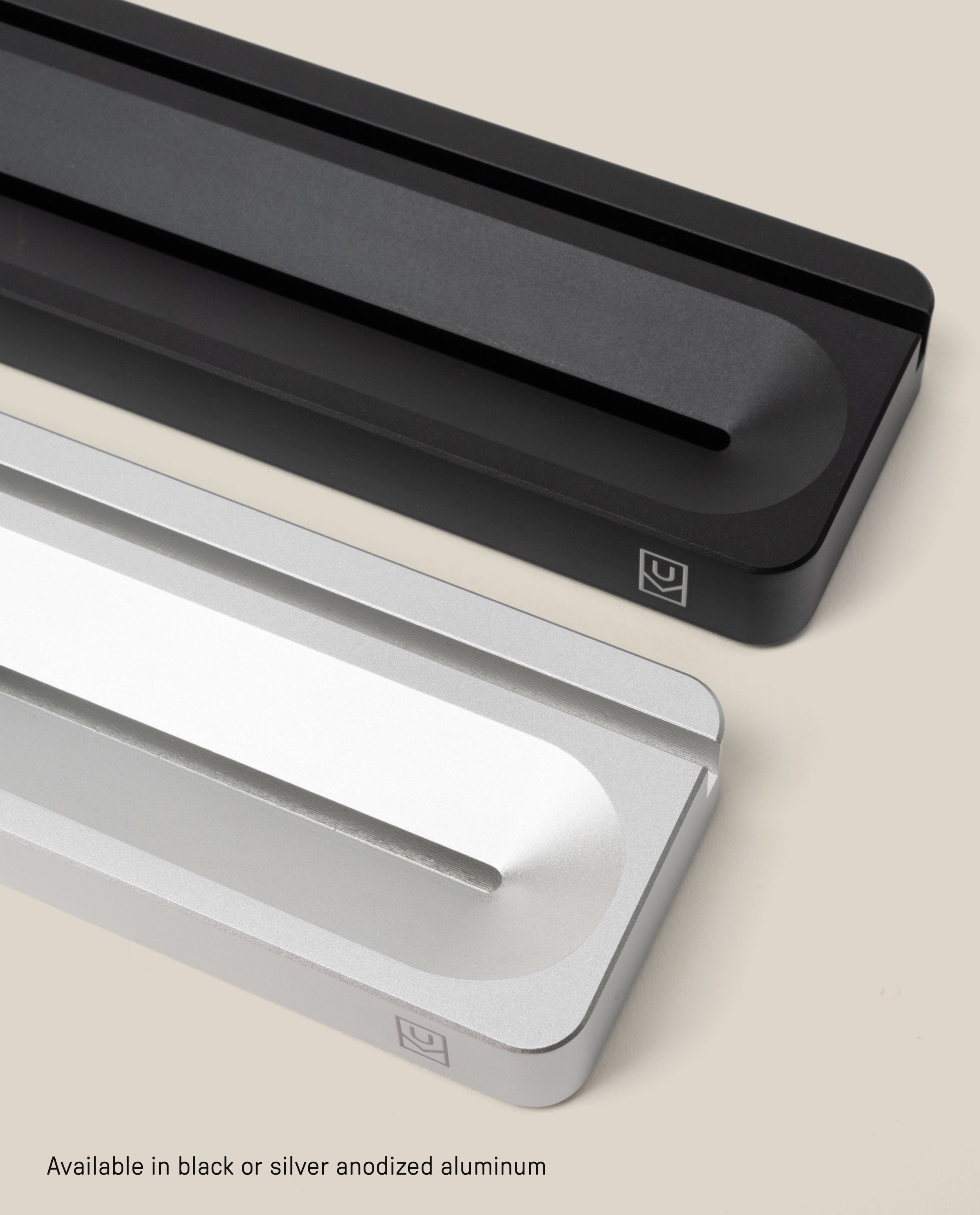 Two minimalist Analog Card Bars (Small 10” – Silver), one in black and one in silver, rest diagonally on a light background. Each solid aluminum stand functions as both a card holder and pen tray, with a central groove and a small corner logo for subtle branding. The text below highlights their availability in black or silver anodized aluminum—making them an ideal desk organizer for modern workspaces.
