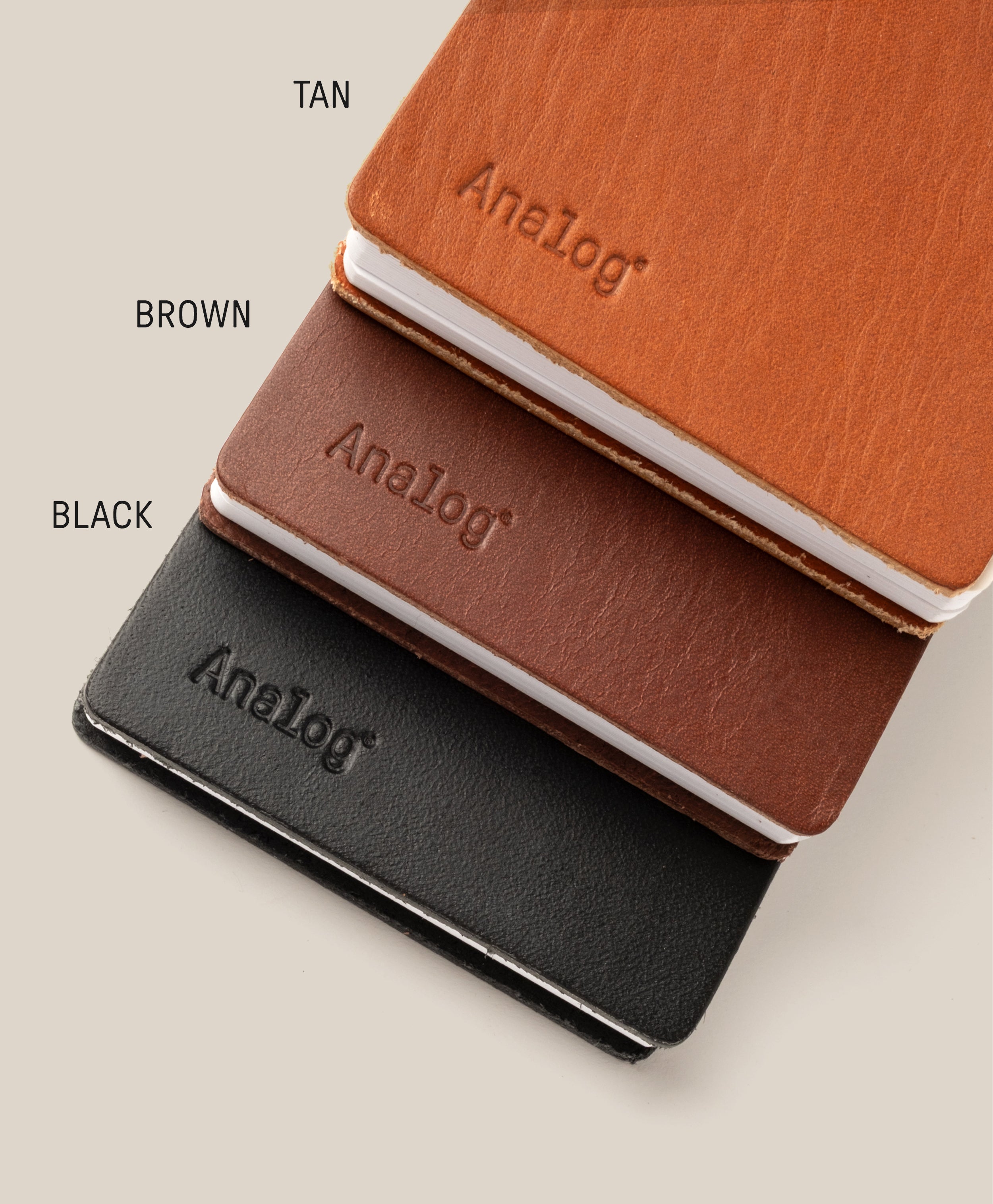 Three Leather Discbound Analog notebooks in tan, brown, and black with full-grain leather covers are stacked diagonally on a beige background. Each has "Analog" embossed on the cover with color labels beside each notebook.