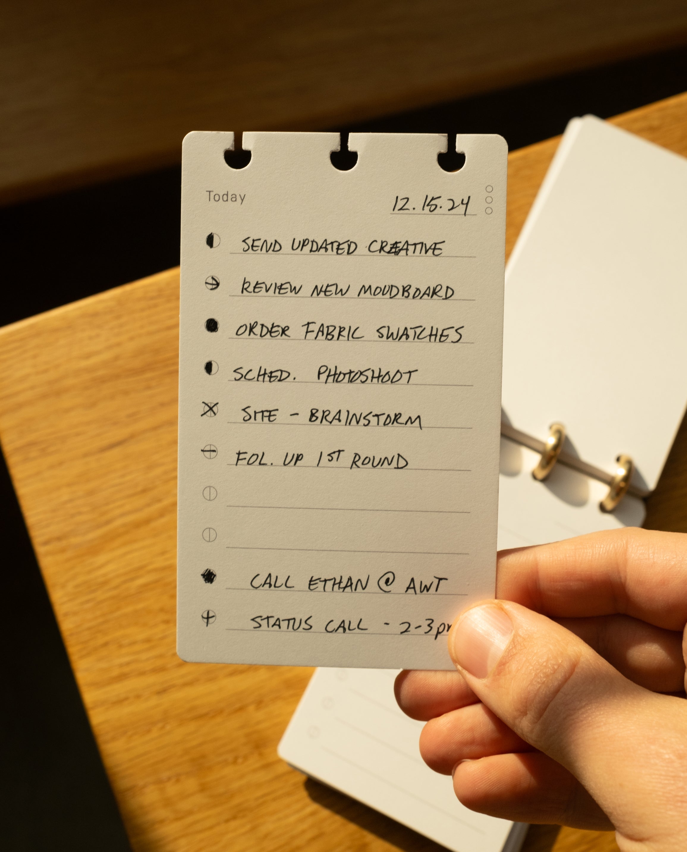 A hand holds a small planner page featuring a to-do list with tasks like sending creative, reviewing a moodboard, ordering swatches, and making calls—some already checked off. The date at the top reads 12.15.24. This page is part of the Discbound Analog system and is shown using the Discbound Analog Refill (6-pack), ideal for organizing your favorite Analog Cards or refreshing your daily productivity setup.