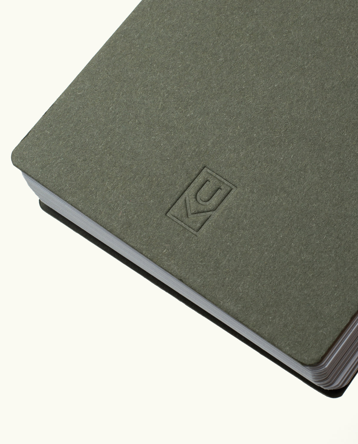 A close-up of the Discbound Analog + 3 Refills notebook in gray-green, featuring a simple embossed KC logo, brass disc binding, rounded corners, and slightly fanned pages against a plain background.