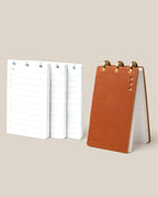 The Leather Discbound Analog + 3 Refills (Tan) features a tan full-grain leather notepad with gold disc rings, shown standing upright beside three stacks of loose refills on a beige background.