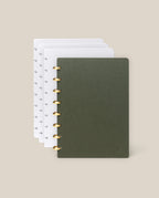 The Discbound Journal Bundle (Standard 6"x 8.5" Journal + 3 Refills) is shown partially open, featuring a dark green cover with gold rings and white dot grid paper, set against a plain beige background.