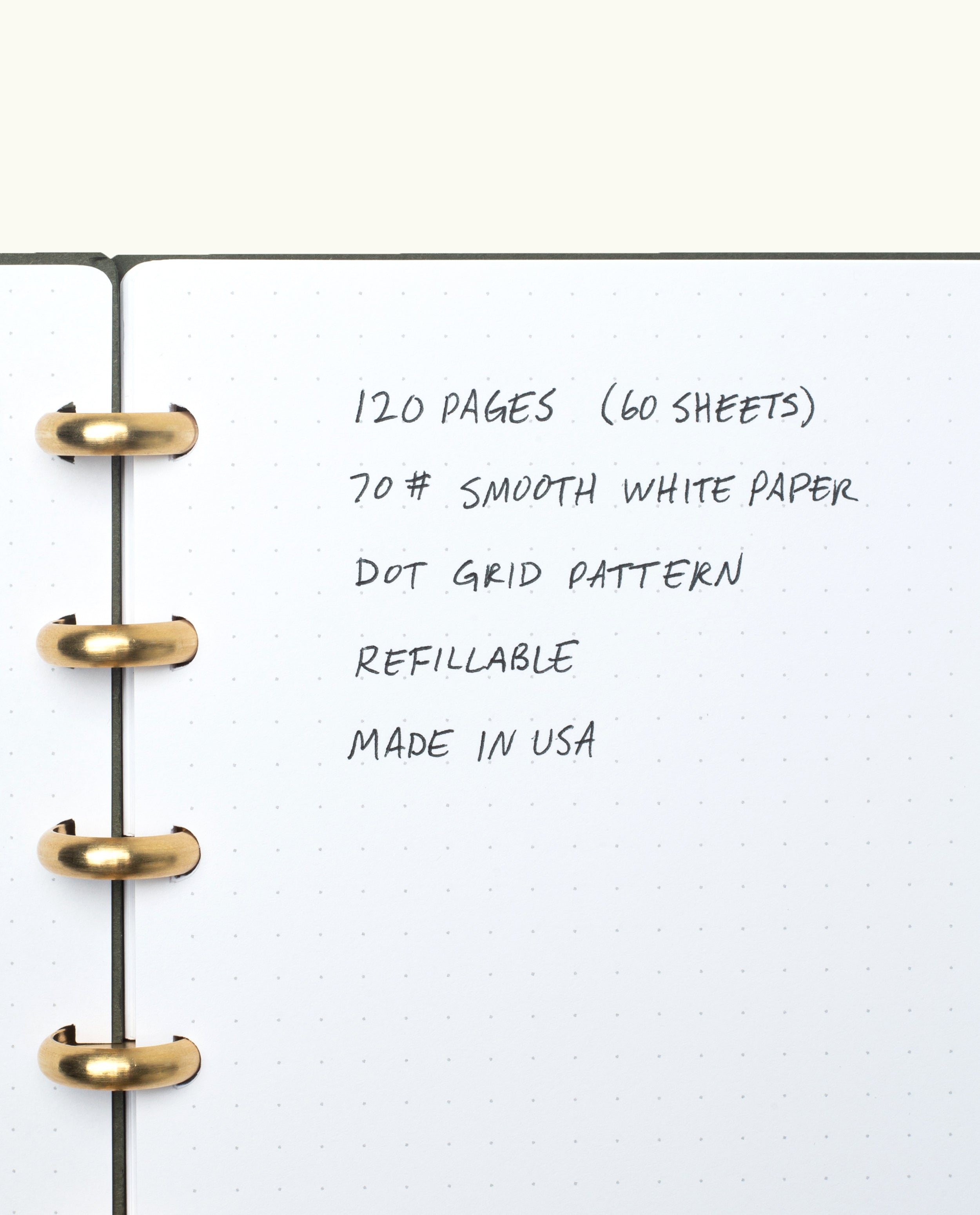 A close-up of the Discbound Journal (Standard 6"x 8.5") with solid brass discs, showing dotted grid pages and handwritten feature notes: 120 pages of 70# smooth white paper, refillable, dot grid pattern, made in USA.