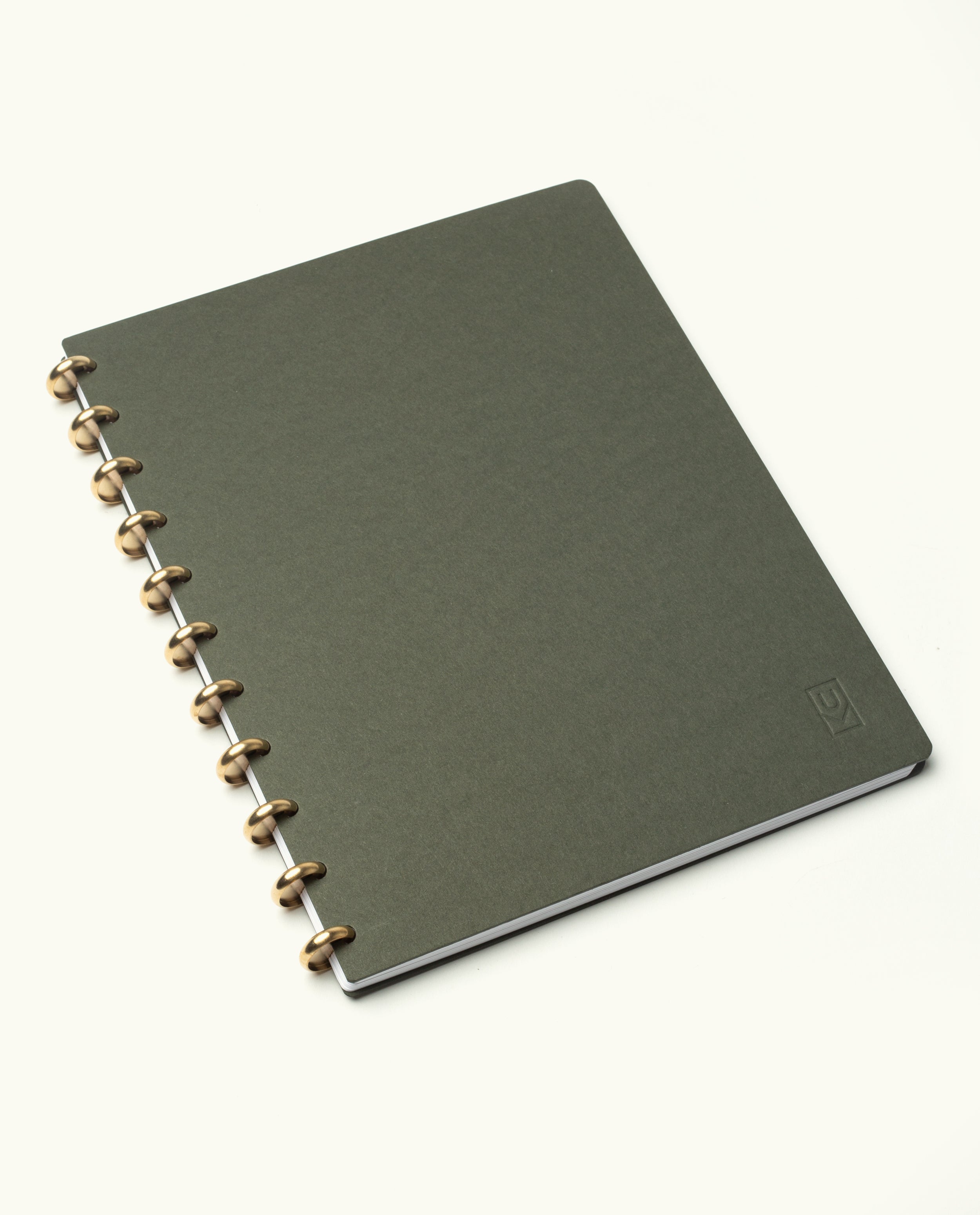 A Discbound Journal Bundle (8.5" x 11" journal plus 3 refills) featuring a closed, dark green refillable notebook with a textured cover and brass disc binding is placed on a white background.