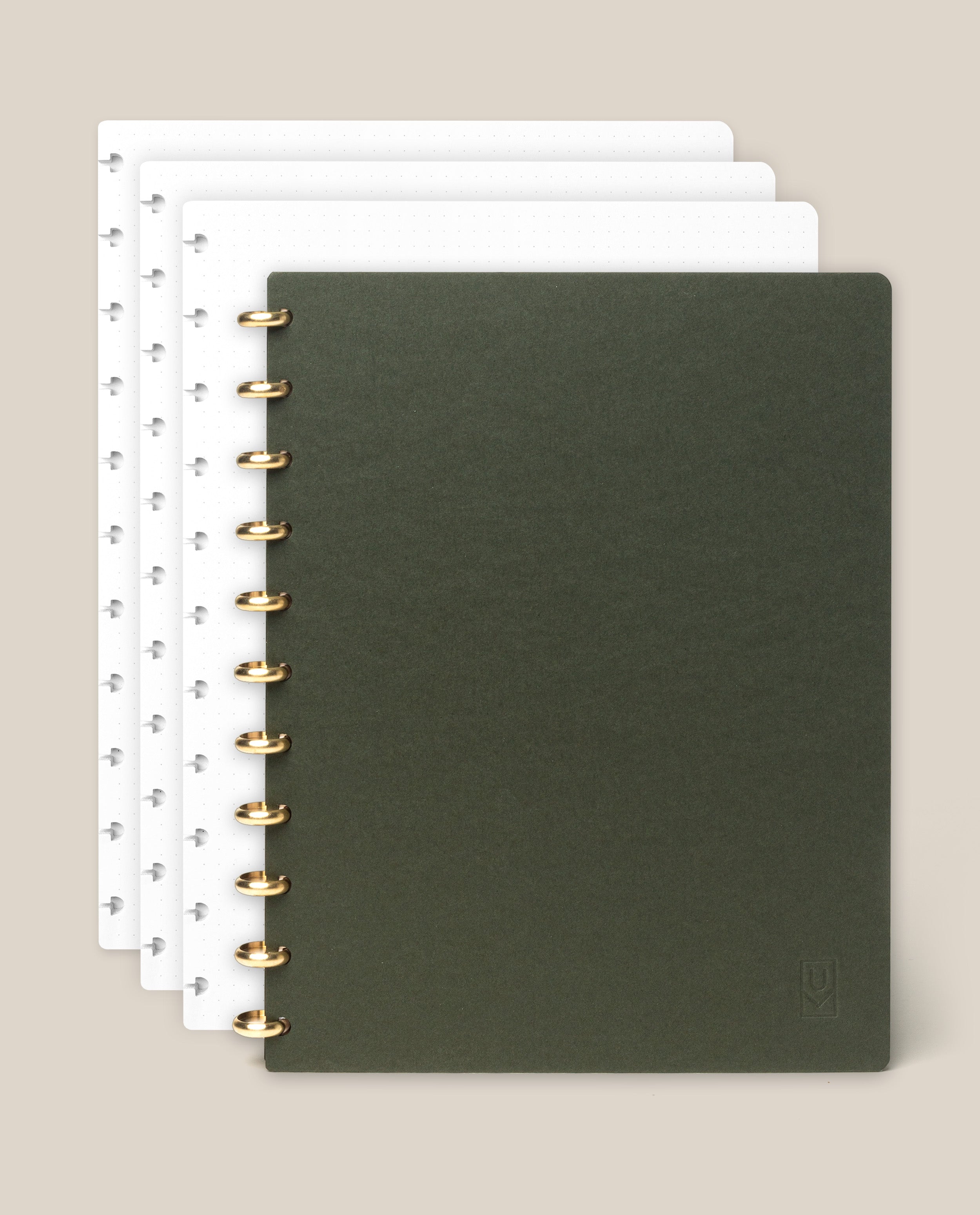 A set of four Discbound Journal Bundles (8.5" x 11" Journal + 3 Refills), each spiral-bound with dotted pages, is arranged in a partially overlapping stack. The top journal displays a dark green cover, while the three beneath it feature white covers. Set against a light beige background, each refillable notebook is elegantly bound with sturdy brass discs for enhanced durability and sophistication.