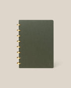 A Discbound Journal (Standard 6"x 8.5") in dark green with brass discs on the left stands upright against a plain beige background.