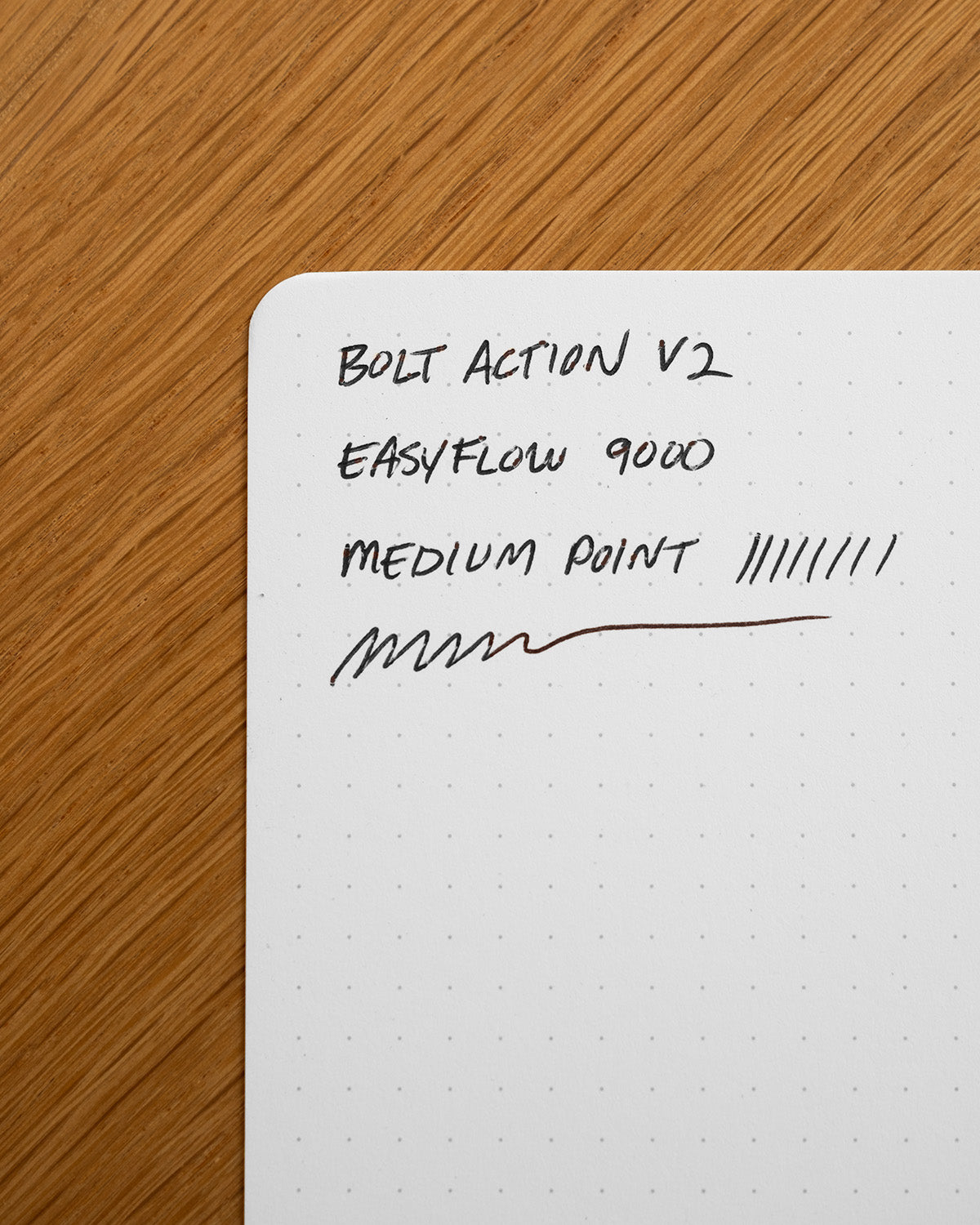 A dotted notebook page on wood with handwritten notes: INVENTERY Bolt Action Pen (Stainless), EASYFLOW 9000, MEDIUM POINT, pen test lines—showing the smooth performance of this Los Angeles-made pen.
