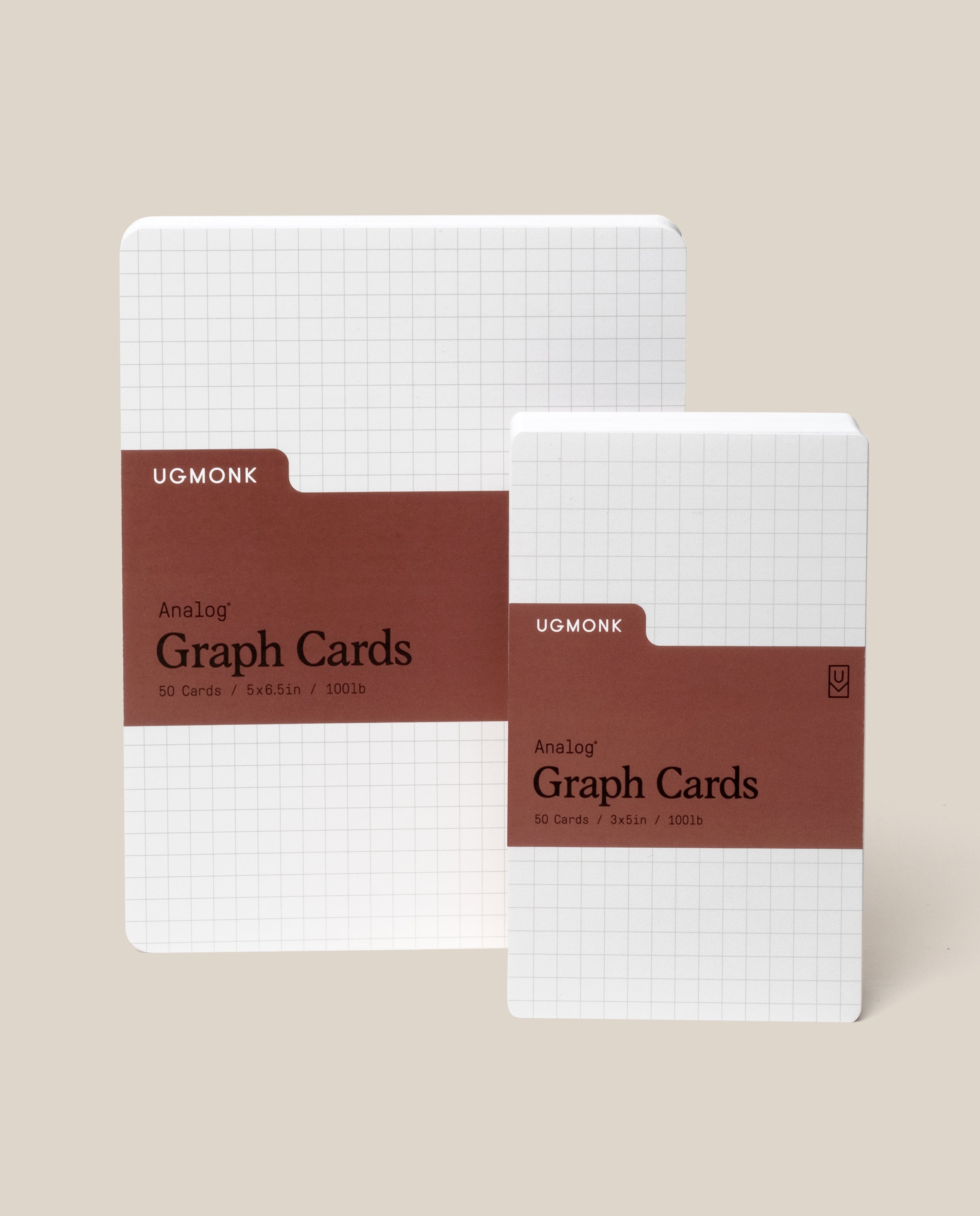 Two packs of Ugmonk Analog Graph Cards are shown upright. Both have a white grid design and a brown label. The larger pack is 5x6.5 inches, the smaller is 3x5 inches. Each contains 50 cards.
