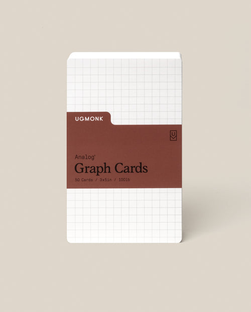 A pack of Analog Graph Cards - Small stands upright, made from uncoated cardstock with a white grid design and a brown label stating: Analog Graph Cards, 50 Cards, 3x5 in / 100 lb. The background is light beige.