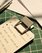 A close-up of a handwritten to-do list secured with HMM Clips (Set of 2 - Raw) to a notepad on a green cutting mat, with a pen and white paper sheets arranged neatly and sunlight illuminating the organized workspace.