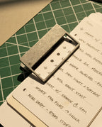 A stack of handwritten to-do lists—meetings, research, updates—is secured by HMM Clips (Set of 2 - Raw) on a green cutting mat as warm sunlight casts gentle shadows across the scene.
