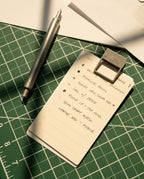 A metal pen and HMM Clips (Set of 2 - Raw) secure a handwritten to-do list on a green cutting mat, with tasks like finalizing a book collection, submitting sales tax, making calls, and sending a draft.