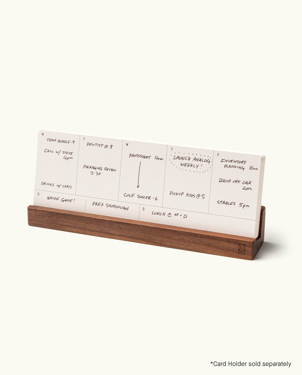 An Analog Weekly Card with a handwritten schedule for meetings and reminders sits in a wooden card holder. Text at the bottom right says, *Card Holder sold separately.