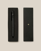 An INVENTERY Bolt Action Pen (Onyx) in matte black, finished with a durable Cerakote ceramic coating for enhanced sophistication and resilience, rests elegantly in a rectangular black gift box lined with foam padding. The box lid is placed beside it on a beige background.