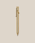 The INVENTERY Bolt Action Pen (Brass), featuring a sleek clip and a smooth bolt-action mechanism, is centered vertically on a plain beige background.