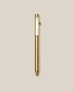 The INVENTERY Bolt Action Pen (Brass) with a clip is centered on a plain beige background. This pen showcases a sleek metallic finish and a simple, modern design, highlighting the durability of its Cerakote ceramic coating.