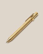The INVENTERY Bolt Action Pen (Brass), featuring a gold metallic finish, a sturdy clip, and a side bolt-action mechanism, is crafted from solid brass and coated with a durable Cerakote ceramic finish. It is displayed on a light beige background.