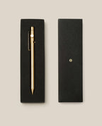 The INVENTERY Bolt Action Pen (Brass), crafted from solid brass and finished with a durable Cerakote ceramic coating, is elegantly presented in a black gift box with its closed lid, set against a beige background.